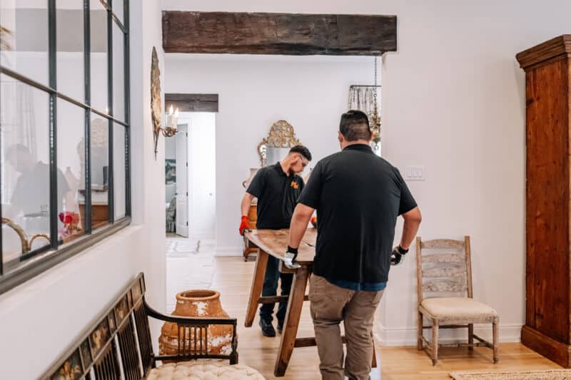 two junkstart junk removal employees moving table inside a san antonio home