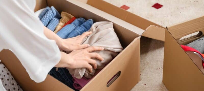 person folding clothes and placing them in a cardboard box