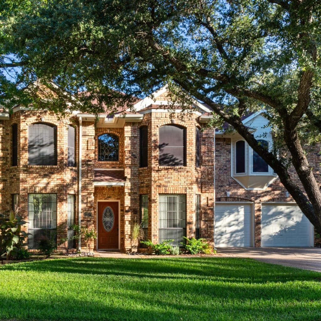 front view of light brown brick home with red front door and two white garage doors