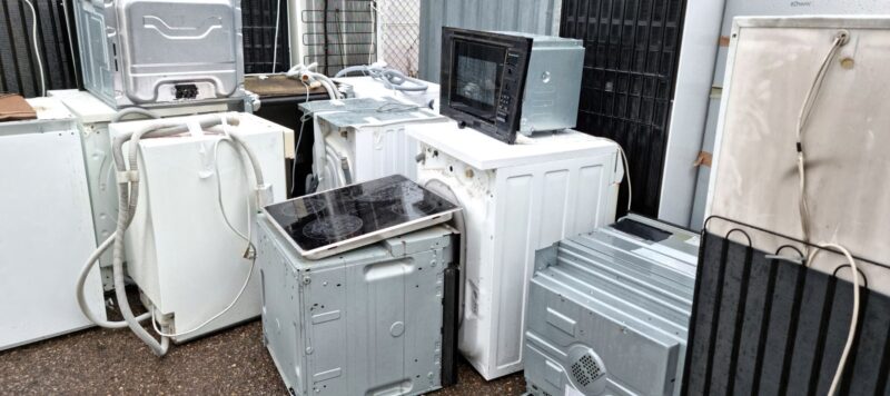 Group of discarded appliances, including washers, microwaves, and stoves, outside