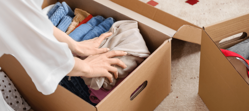 hands pushing clothes into a box to pack away