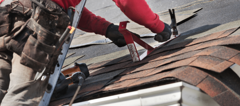 technician up on the roof adding asphalt shingle roofing material