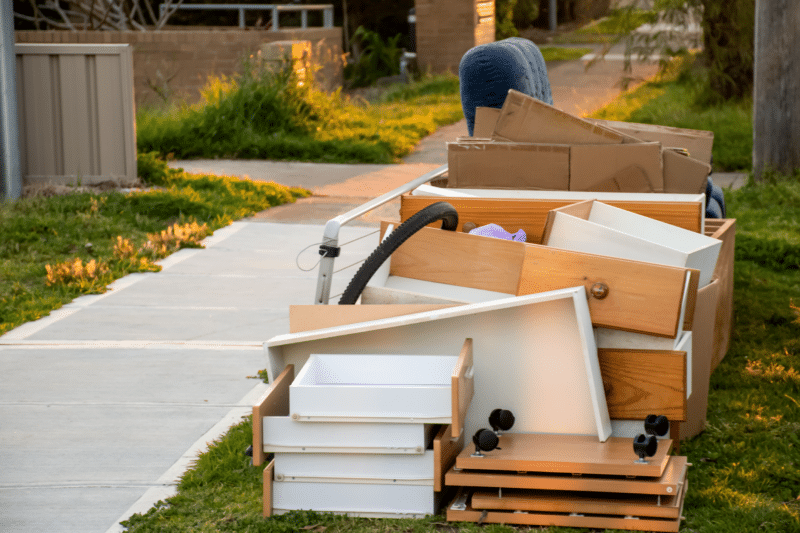 pile of boxes and other items set by the sidewalk outside of a home