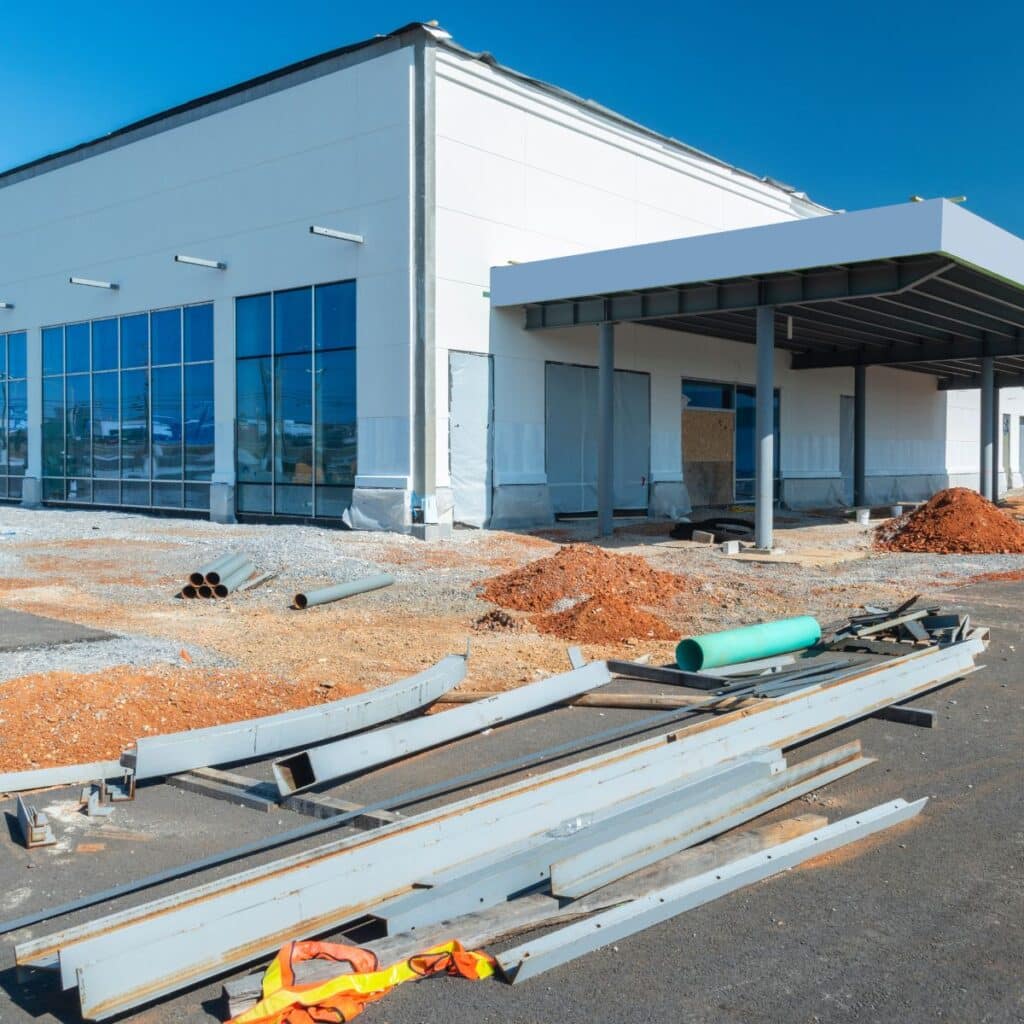 A commercial building under construction with scattered steel beams and dirt piles