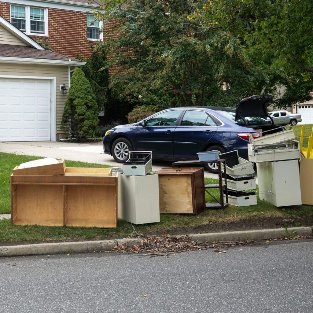 Assorted furniture and household items placed on the curb in front of a suburban home