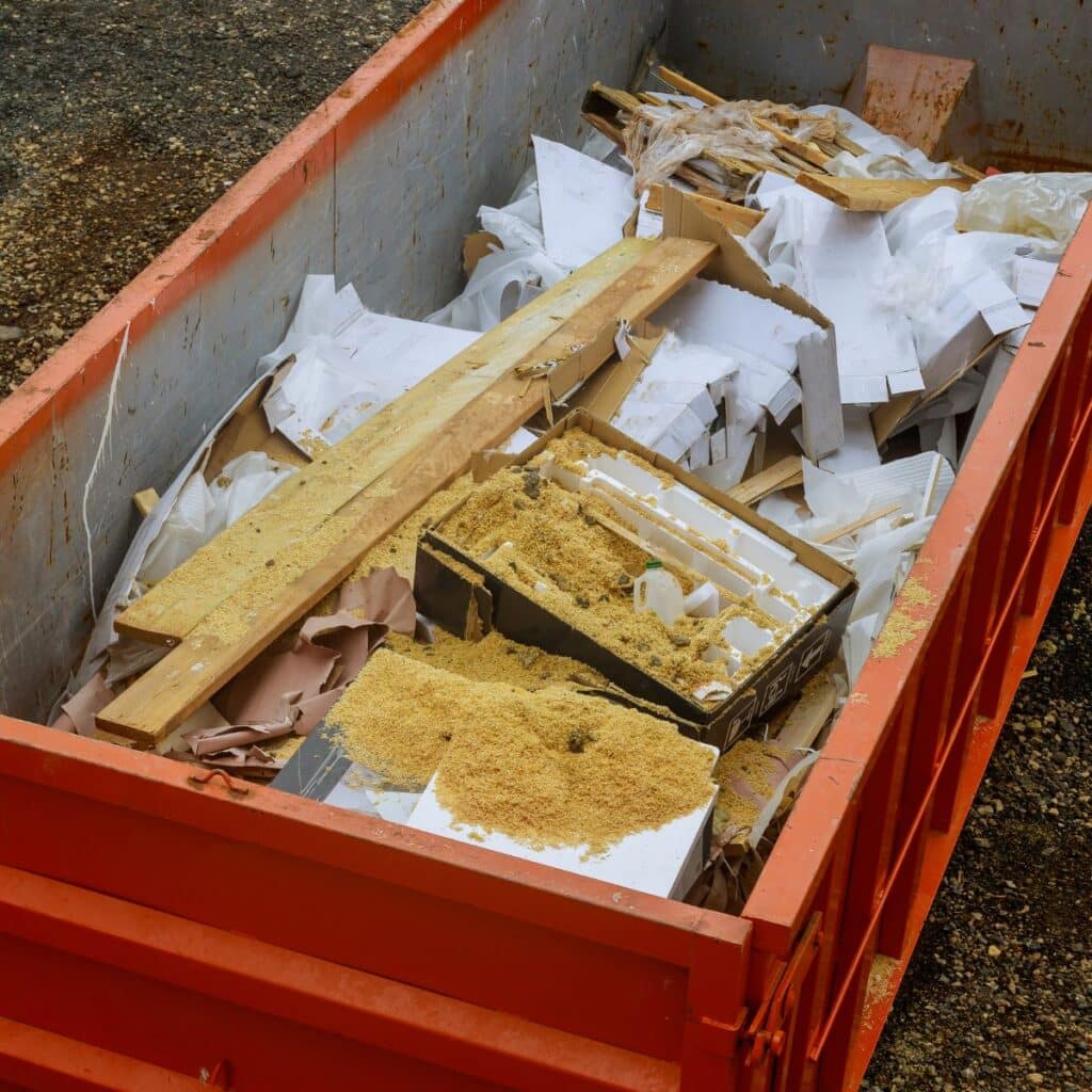 A large red dumpster filled with renovation debris, including sawdust, wood, and packaging