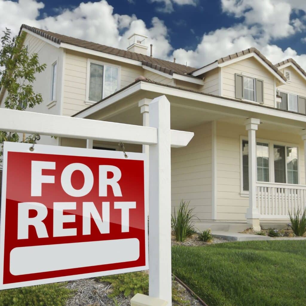 A red and white “For Rent” sign in front of a two-story beige suburban home with a manicured lawn