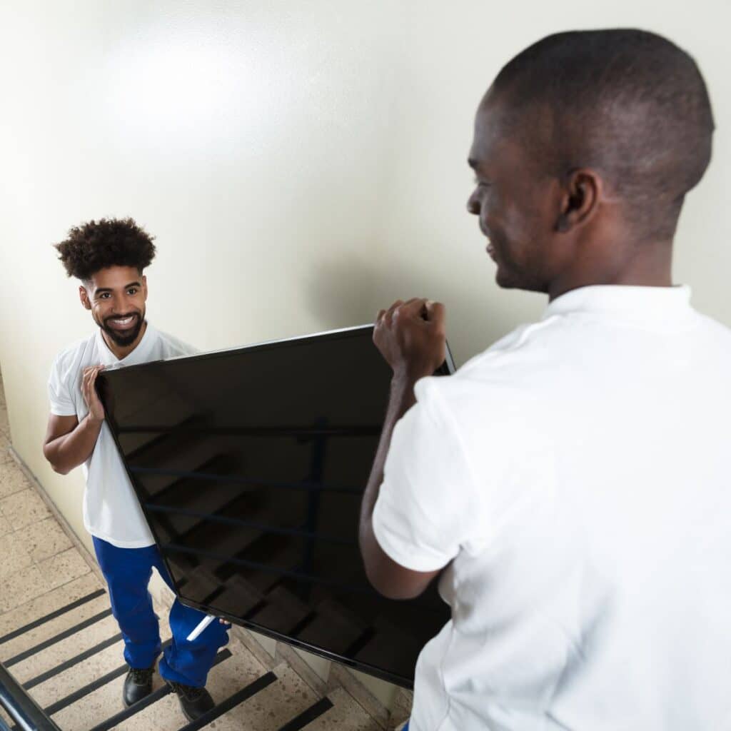 Two men carefully carrying a large flat-screen TV down a stairwell