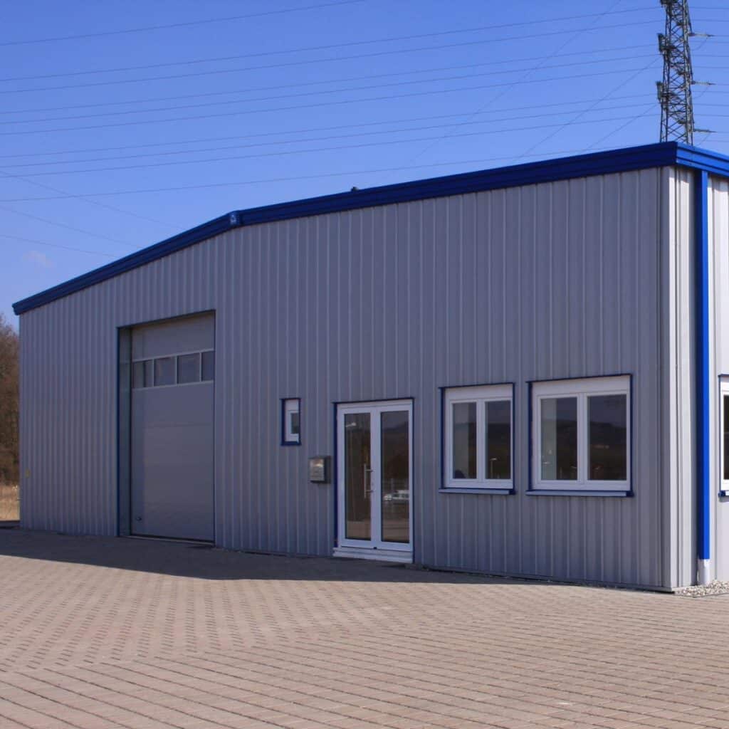 Exterior view of a metal warehouse building with multiple windows and a large roll-up door