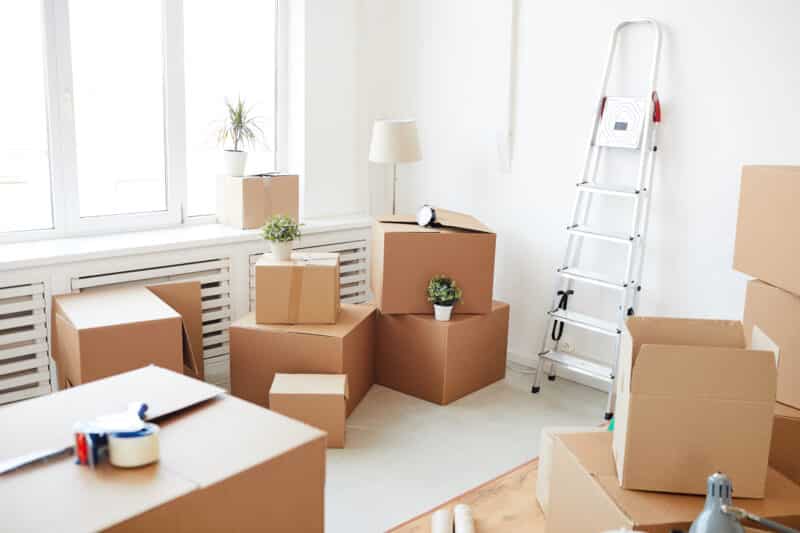 Wide angle background of stacked cardboard boxes in empty white room, moving, relocation and house decor concept